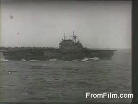 The still captures the USS Hornet, an aircraft carrier, at sea during the Doolittle Raid on April 18, 1942. The ship is shown in profile, with sailors visible on deck, as B-25 bombers prepare for their historic launch. The black-and-white image evokes a sense of wartime urgency and highlights the carrier's pivotal role in this significant military operation.