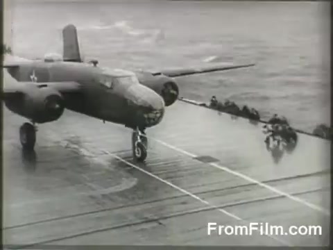 The still captures a B-25 bomber positioned on the flight deck of the USS Hornet, preparing for launch during the Doolittle Raid on April 18, 1942. The ocean is visible in the background, emphasizing the aircraft's precarious launch from an aircraft carrier. Crew members can be seen observing the takeoff, highlighting the tension and significance of the historic mission. The image reflects a moment of determination in a pivotal World War II event.