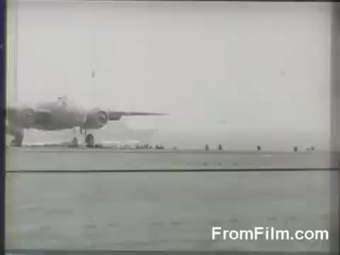 The still depicts a B-25 bomber taking off from the deck of the USS Hornet during the Doolittle Raid on April 18, 1942. The aircraft is shown in mid-launch, with crew members visible preparing for takeoff. The scene captures the tense atmosphere and significant moment in U.S. military history.