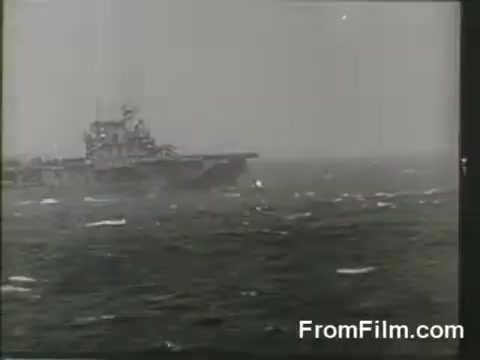 The still depicts the USS Hornet, a military aircraft carrier, amidst rough seas. It captures the moment of the Doolittle Raid, highlighting the launch of B-25 bombers on April 18, 1942. The gray, overcast atmosphere and choppy waters convey the challenging conditions faced by the raiders during this pivotal mission.