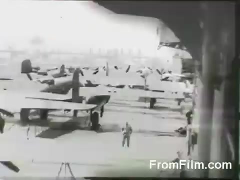 The still shows multiple B-25 bombers lined up on the deck of the USS Hornet, preparing for the Doolittle Raid on April 18, 1942. Personnel are visible in the foreground, coordinating the launch of the aircraft. The context highlights a pivotal moment in WWII, where these bombers took off on a daring mission to strike Japan.