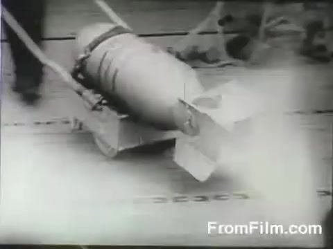 The still depicts a large bomb being maneuvered on a trolley, likely on the deck of the USS Hornet. This scene is set during the Doolittle Raid on April 18, 1942, showcasing the preparations for the historic airstrike as B-25 bombers were launched. The atmosphere is tense, highlighting the urgency and significance of the mission.