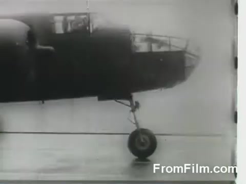 The still depicts a B-25 bomber, part of the Doolittle Raid, poised for launch from the USS Hornet on April 18, 1942. The aircraft is captured in profile, emphasizing its distinctive design and landing gear, set against a blurred background that likely represents the aircraft carrier's deck. The moment highlights the urgency and significance of this historic military operation.