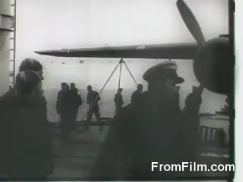 The still captures a moment aboard the USS Hornet during the Doolittle Raid on April 18, 1942. In the foreground, sailors, some in military uniforms and caps, are seen moving about the deck near the B-25 bombers being prepared for launch. A propeller is visible, indicating the aircraft's readiness. The overall scene conveys a sense of urgency and teamwork as they prepare for the historic air raid on Japan.