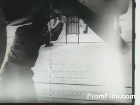 The still depicts a crew member working on a B-25 bomber, likely preparing for takeoff from the USS Hornet during the Doolittle Raid on April 18, 1942. The setting appears to be an aircraft carrier deck, showing the bustling activity involved in launching the mission. The image captures a moment of urgency and teamwork amidst the historic air raid preparation.