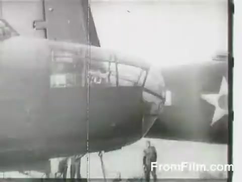 The still shows a close-up of a B-25 bomber on the USS Hornet, capturing the moment before the Doolittle Raid on April 18, 1942. Ground crew members are visible near the aircraft, which features military insignia, highlighting the historical significance of this daring air raid against Japan during World War II.