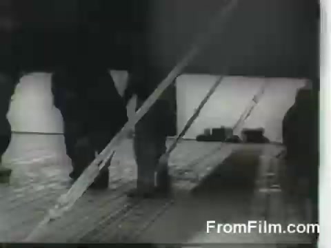 The still shows individuals on the deck of the USS Hornet, preparing for the launch of B-25 bombers during the Doolittle Raid on April 18, 1942. The scene likely captures the tense atmosphere and urgency of military preparations, with figures moving along the deck among visible aircraft-related equipment.