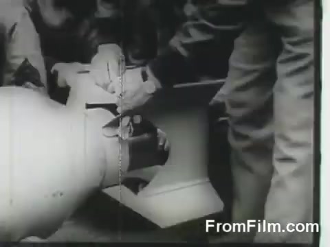 The still captures a moment during the Doolittle Raid, showing crew members preparing a bomb or ordnance on a B-25 bomber. The focus is on their hands as they work diligently, emphasizing the tension and urgency of the mission as the aircraft are readied for launch from the USS Hornet on April 18, 1942. The black-and-white imagery reflects the historical context of World War II.