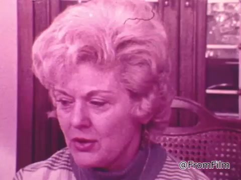 The still features a woman with light, wavy hair, appearing thoughtful or concerned. She is seated, with a woven chair visible behind her. The color tone of the image is warm, possibly giving it a vintage feel. This reflects the intimate and personal nature typical of public service announcements, likely emphasizing themes of compassion and community support related to the 'One Great Hour of Sharing' initiative.