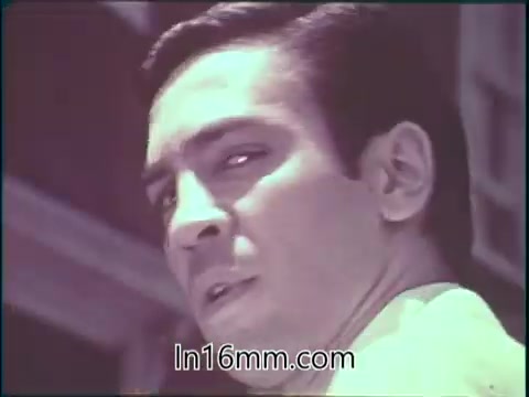 The still from 'State Employment Service PSA - Pitching Pennies' features a man with a serious expression, looking over his shoulder. The image captures a moment of contemplation or concern, likely reflecting the themes of employment challenges depicted in the PSA. The overall aesthetic is typical of 16mm film, suggesting a vintage quality. The context hints at a message regarding employment services and support.