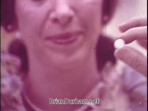 The still from the Phillips Milk of Magnesia commercial features a woman holding a small white pill close to her face. The image has a soft focus with a color palette typical of the 1970s. The woman appears to be demonstrating the product, likely promoting its benefits.   Regarding the reference to Flo from 'Alice,' Polly Holliday, who portrayed Flo on the show, did appear in various commercials during that era, but without seeing more context, it's uncertain if this is indeed her.