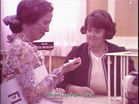 The still features two women in a commercial for Phillips Milk of Magnesia. One woman is holding a bottle, and they appear to be engaged in a conversation at a counter. The setting has a retro vibe, typical of the 1970s, with floral patterns and pastel colors. The woman on the left could be Polly Holliday, who is known for her role as Flo in the TV series 'Alice.' The commercial seems to highlight the product in a friendly and relatable manner.