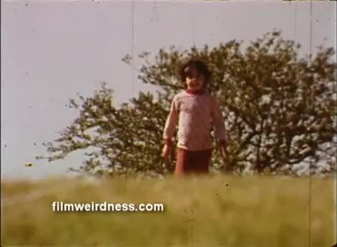 The still shows a young child walking through a grassy field, with a large tree in the background. The scene conveys a sense of innocence and joy, typical of public service announcements aimed at highlighting the mission of St. Jude's Children's Research Hospital. The colors and quality suggest a vintage aesthetic, likely from the era in which the PSA was filmed.