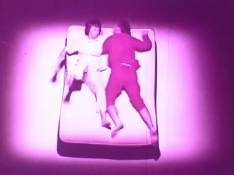 The still from the 'Beautyrest Mattress Commercial' features two people on a mattress. They appear to be playfully moving around, highlighting the mattress's comfort and support. The image is illuminated with a purple hue, creating a whimsical and engaging atmosphere.