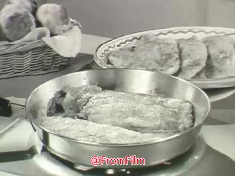 The 16mm still from the 'Chase & Sanborn Coffee' and 'Blue Bonnet Margarine' commercial features a frying pan with what appears to be several pieces of food being cooked, possibly coated with margarine. In the background, a basket with rolls is visible alongside a plate of what looks like fried items. The scene is shot in a vintage style typical of the 1960s, highlighting themes of home cooking and quality ingredients, reinforced by the voice-over emphasizing the legacy and care in the coffee brand's roasting process.