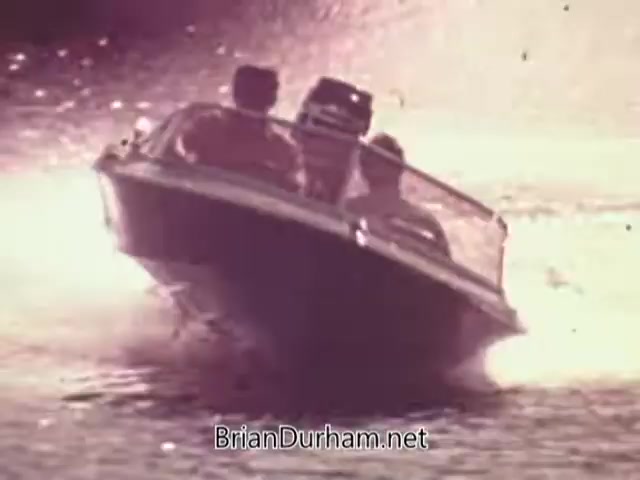 The still features a speedboat gliding over water, spraying water in the air, showcasing a lively scene typical of 1960s recreational boating. In the boat, there are several individuals enjoying the ride, emphasizing the thrill and leisure associated with Mercury outboard engines. The setting captures a sunny, bright atmosphere, highlighting the appeal of boating at the time.