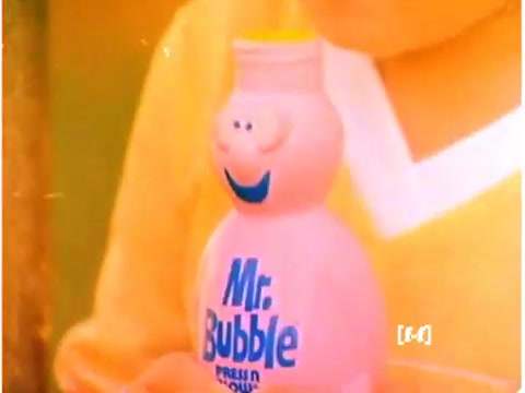The still features a close-up of a pink bottle of Mr. Bubble, characterized by its cartoonish smiling face and blue label. The bottle is held in the hands of a child, who is partially visible in a yellow sweater. The colors appear faded and yellowed, a common issue with older CRI film negatives. The overall tone conveys a nostalgic atmosphere typical of 1970s commercials.