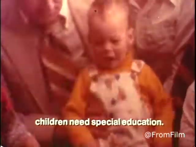 The still from the 16mm film features a young child, dressed in an orange shirt and patterned overalls, being held by an adult. The child appears attentive, while the adult figures surrounding them are focused and engaged. At the bottom, the text states, 'children need special education,' highlighting the film's message from the 1970s Parents' Campaign for Handicapped Children and Youth. The overall tone suggests an emphasis on support and advocacy for children with disabilities.