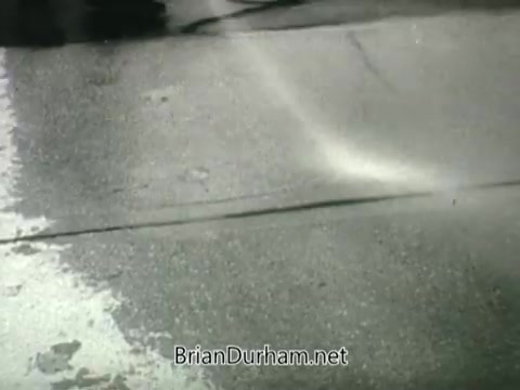 The still from the Public Health Service Clean Air PSA depicts a street scene with a focus on pavement that appears wet or treated. The image emphasizes surface cleanliness, likely as part of a broader message promoting clean air and public health. The black-and-white aesthetic typical of the 1960s lends a historical feel to the visual, aligning with the era's public health campaigns.