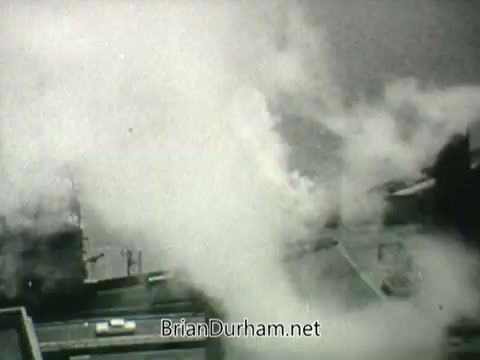 The still from the 'Public Health Service Clean Air PSA - 1960s' depicts a scene of industrial activity with visible smoke and pollutants being released into the air. The grayscale imagery suggests a stark, serious tone, highlighting the environmental concerns of the time. The focus on smoke emphasizes the message about air quality and public health issues.