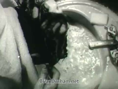 The still from the 'Public Health Service Clean Air PSA - 1960's' features a close-up view of someone's hands submerged in large, bubbling water, possibly in a sink. The scene emphasizes the importance of cleanliness and, by extension, clean air as part of public health messaging. The black-and-white format contributes to the vintage look typical of that era's public service announcements.