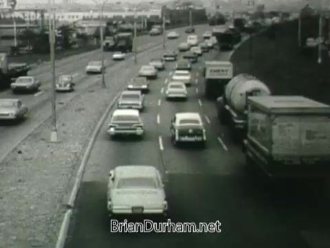 The still from the 1960s Public Health Service Clean Air PSA depicts a busy roadway filled with cars and trucks. The scene is likely meant to illustrate traffic pollution and its impact on air quality. The monochromatic tone adds a vintage feel, emphasizing the era's concerns about environmental health.