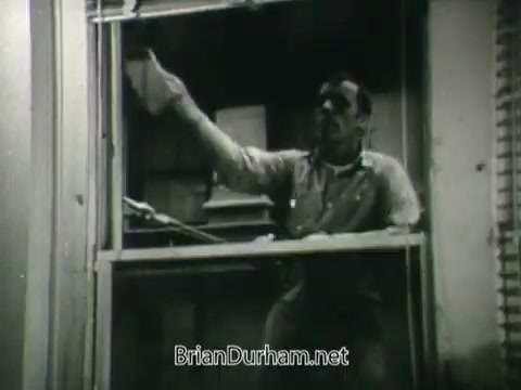 The still from the 'Public Health Service Clean Air PSA - 1960's' features a man leaning out of a window, presumably engaged in cleaning or maintaining the exterior. The black-and-white imagery emphasizes the focus on public health and cleanliness, reflecting the PSA's message about the importance of clean air during that era. The setting suggests a domestic environment, linking individual actions to broader public health initiatives.