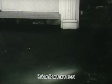 The still from the 'Public Health Service Clean Air PSA - 1960s' depicts a dimly lit area, possibly indoors, focusing on the floor beneath a piece of furniture. The scene is likely meant to emphasize the importance of clean air and the impact of pollution, with a somber tone suggesting neglect or consequences related to air quality. The visual composition highlights a sense of stillness, possibly inviting viewers to reflect on their environment and health.