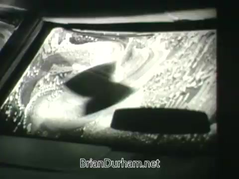 The still from the 'Public Health Service Clean Air PSA' shows a close-up view of a car windshield being cleaned. The scene features a mixture of water and soap suds, highlighting the importance of clean air visibly affecting the clarity of the glass. The imagery conveys a message about air quality and its impact on health and visibility.