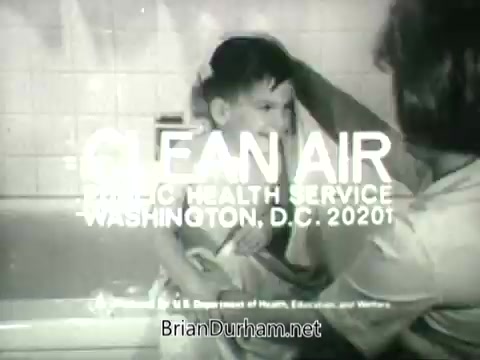 The still features a child being bathed, with a caregiver gently washing their hair. Overlaid text states 'CLEAN AIR PUBLIC HEALTH SERVICE WASHINGTON, D.C. 20201.' The image emphasizes the importance of clean air for health and well-being, consistent with the PSA's focus on public health. The imagery conveys a nurturing scene that connects personal care to broader environmental health issues.