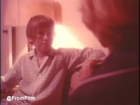 The still from the 1974 trailer of 'Alice Doesn't Live Here Anymore' features a scene with a young man in glasses, dressed in a checked shirt, engaged in conversation. The warm, soft lighting creates an intimate atmosphere. The focus is on the interaction, suggesting a moment of personal connection. The film, starring Ellen Burstyn, addresses themes of resilience and the quest for identity. The accompanying music by Mott The Hoople adds a nostalgic touch to the trailer.