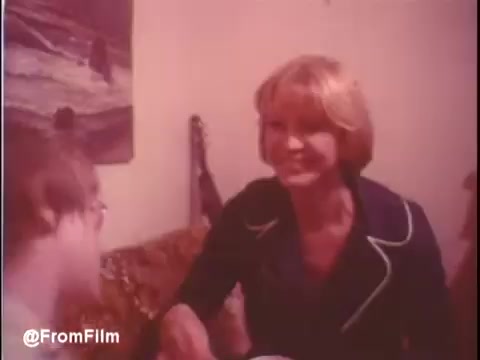 The still from the trailer of 'Alice Doesn't Live Here Anymore' (1974) features a scene likely reflecting the film's intimate, personal moments. Ellen Burstyn is shown engaging with another character in a cozy, domestic setting. The warm, soft lighting and vintage color palette evoke a sense of nostalgia. The film's theme of personal struggle and resilience is underscored by the lighthearted interaction, complemented by the upbeat music from Mott The Hoople playing in the background.