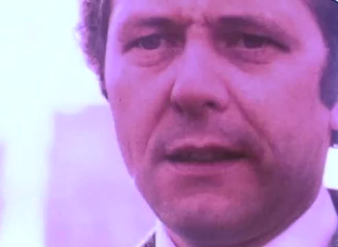 The still from the 'Hire An Ex-Offender PSA' features a close-up of a man with a serious expression. He appears to be addressing an audience or camera, conveying a message of importance related to the theme of rehabilitation and employment for ex-offenders. The colors are muted, characteristic of 16mm film, emphasizing the somber tone of the subject matter.