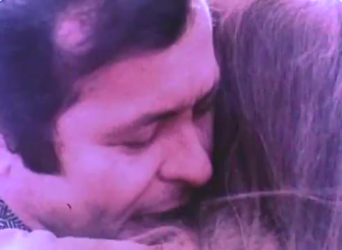 The still from the 'Hire An Ex-Offender PSA' shows a tender moment between a man and a woman, likely featuring an emotional reunion. The man's expression conveys a sense of relief and joy, while the woman appears to be embracing him warmly. The soft focus and color palette typical of 16mm film suggest a nostalgic tone, underscoring the personal and human aspect of the message surrounding reintegration and support for ex-offenders.