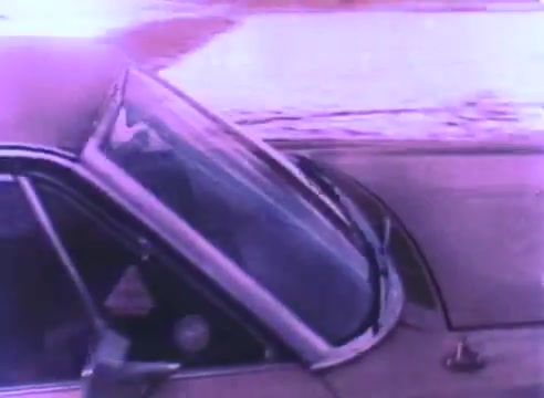 The still from the 'Hire An Ex-Offender PSA' showcases a close-up of a car, emphasizing the windshield and side view. The image is characterized by a vintage aesthetic typical of 16mm film, with a slight purple tint. It suggests themes of movement and transition, likely tying into the broader message of reintegration and second chances for ex-offenders.