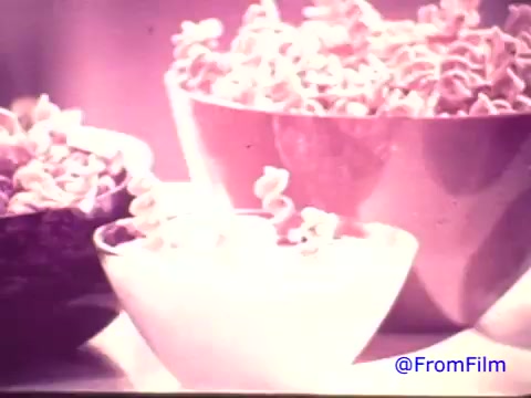 The still from the 16mm print of 'Nabisco Korker Corn Twists - 1970's' showcases various bowls filled with the snack. The colors have faded, transforming the original red tones to a monochrome appearance, likely giving it a nostalgic feel. The prominent focus is on the curly, twisted corn snack, which appears inviting and playful in shape. Overall, the image captures the essence of a short-lived snack chip from that era.   .