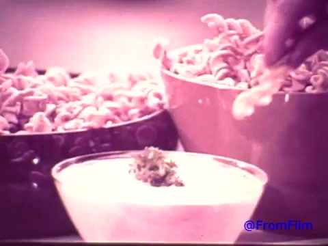 The still from the 16mm print features a hand reaching towards a bowl of Nabisco Korker Corn Twists, with two large bowls of the snack in the background. The image has a faded quality, shifting from its original red tint to a black and white appearance, capturing a nostalgic vibe of the early 1970s. In the foreground, a dip with a green garnish is showcased, emphasizing the snack's intended consumption context. The overall composition reflects the casual and inviting atmosphere of the era's snack culture.