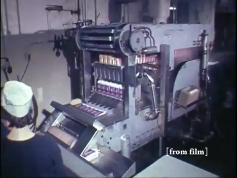 The still shows a vintage industrial setup from 1967, featuring a large, intricately designed machine used for producing ice cream novelties. In the foreground, an operator wearing a cap is attentively monitoring the machine's operation. The machine itself is equipped with multiple tubes and rollers, likely for filling molds or containers with ice cream. The scene conveys a sense of nostalgia, highlighting the manufacturing process of frozen treats during that era. The color quality of the Kodachrome film adds a warm, vibrant tone, characteristic of its time.