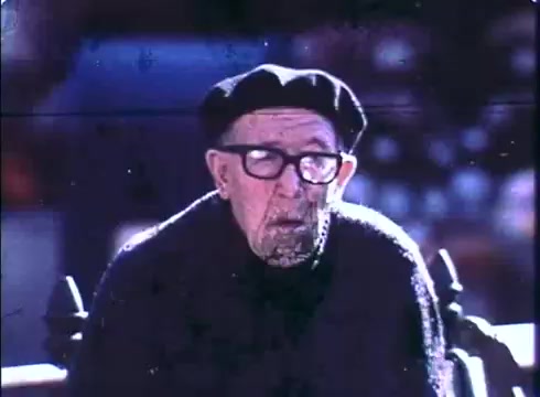The still features a weathered older man wearing glasses and a black beret, sitting on a bench. He has a thoughtful expression, conveying a sense of wisdom and age. The color tones are slightly faded, typical of a 16mm print, adding a nostalgic feel to the image. This captures a moment that reflects the film's themes of aging and companionship.