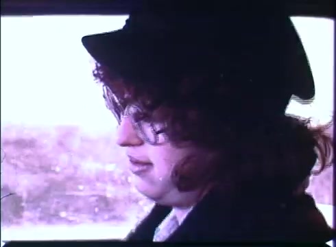 The still shows a character with curly hair and glasses, wearing a hat, sitting in a car. The background suggests a snowy or wintry landscape. The mood appears contemplative, fitting the reflective tone of 'Harry and Tonto.' The 16mm print offers a vintage aesthetic, characteristic of older film formats.