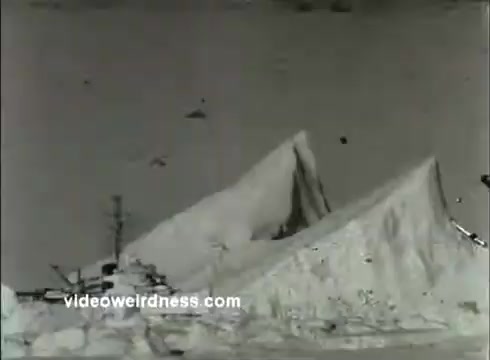 The still from the 1950s Coast Guard Academy PSA depicts a large ice formation or glacier, potentially in a coastal or arctic environment. In the foreground, there may be industrial equipment or vessels, suggesting a connection to maritime activities. The image conveys a sense of ruggedness and the challenges faced by the Coast Guard in marine and icy conditions. The overall tone is likely serious, emphasizing the Coast Guard's mission.