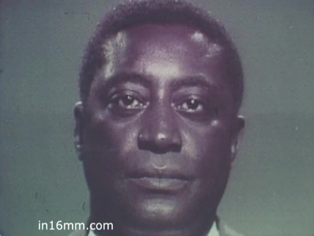 The still from 'The Turning Point PSA - 1960s' features a close-up of a man with a serious expression. His face is illuminated against a neutral background, emphasizing the gravity of the message. The image conveys a sense of urgency and importance, typical of public service announcements from that era.