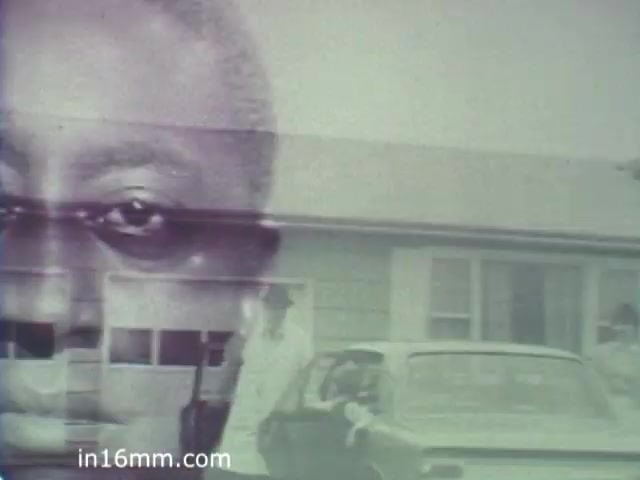 The still features a prominent close-up of a man's face, possibly conveying a sense of intensity or contemplation. In the background, there's a suburban house and a car, suggesting an everyday context. The juxtaposition of the facial image with the setting may evoke themes of personal or societal challenges, likely pertinent to the message of the 'Turning Point' PSA from the 1960s. The overall composition hints at a narrative involving individuals and their environments, reflecting broader social issues.