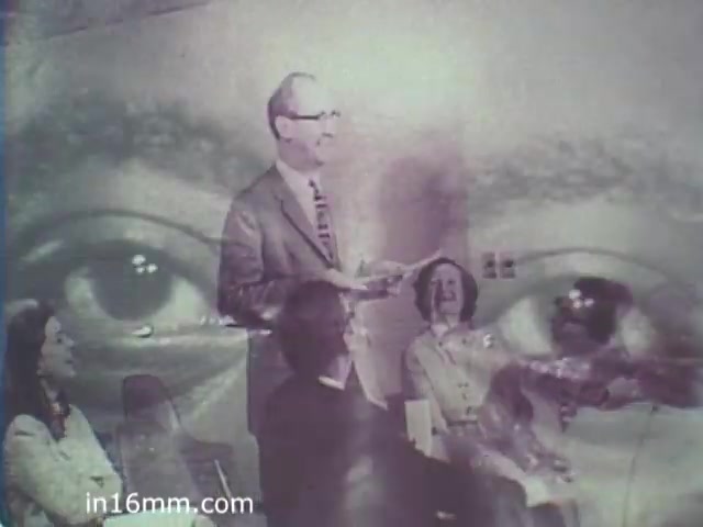 The still features a multi-layered image, prominently showing a man in a suit speaking, likely at a meeting or presentation. He appears engaged and animated. In the background, there's an overlay of large, expressive eyes, suggesting a theme of awareness or introspection. A group of people, including women and men, are seated and seemingly attentive, creating an inclusive atmosphere. The visual style reflects a retro vibe characteristic of the 1960s.