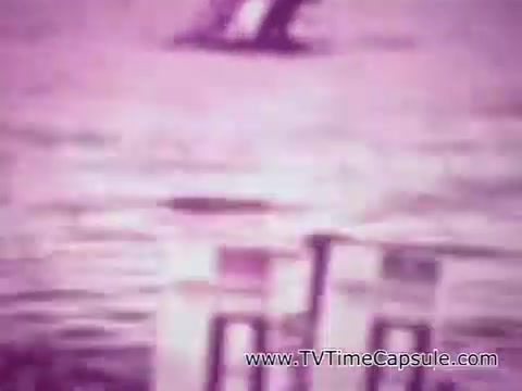 The still from the Listerine Breath Spray commercial in 16mm format features a soft, washed-out color palette with a dominant pink hue. The focus appears to be on two spray bottles positioned prominently in the foreground, suggesting a product advertisement. The background is blurry and indistinct, providing a nostalgic and vintage feel to the image. Overall, it captures a moment typical of mid-20th century advertising aesthetics.