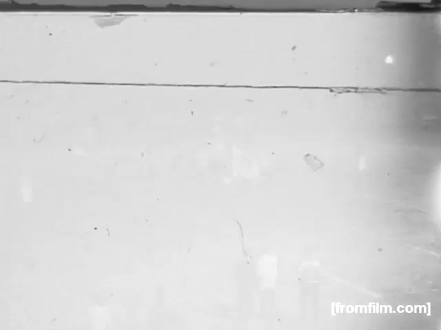 The still from 'High School Football - 1961' likely captures a moment from a football game, showcasing players in action on the field. The image may display elements typical of that era, such as vintage uniforms and possibly a small crowd in the background. The film appears aged, with visible artifacts like scratches and dust, adding a nostalgic quality to the scene. The specific teams and location are unknown.