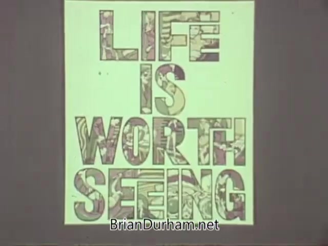 The still features a bold, colorful typographic display that reads 'LIFE IS WORTH SEEING.' The letters are filled with intricate patterns, emphasizing the message's importance. The background is minimal, allowing the text to stand out, likely conveying a positive and impactful message about vision and the value of life experiences. This piece is part of a public service announcement from the American Optometric Association in the 1960s.