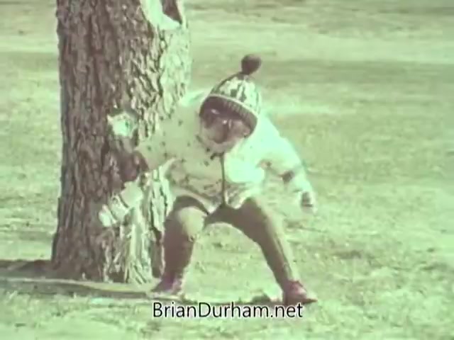 The still features a child squatting near a tree in a park setting, wearing a winter coat with a patterned hat. The child appears to be engaging with their surroundings, possibly playing or observing something on the ground. The imagery evokes a playful, innocent atmosphere typical of 1960s public service announcements.
