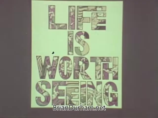 The still features a bold, graphic design with the phrase 'LIFE IS WORTH SEEING.' The letters are creatively filled with colorful, patterned imagery, conveying a message about the importance of vision and appreciating life's experiences. The background is likely a muted or plain color, emphasizing the text. This visual is part of a public service announcement by the American Optometric Association from the 1960s.