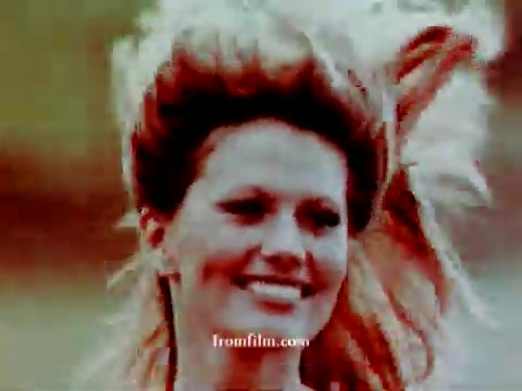 The still features a woman smiling, with her hair styled in a dramatic, voluminous manner. The colors appear warm and slightly faded, characteristic of vintage film, likely reflecting the era of the 1972 Volkswagen commercial. The background is blurred, emphasizing the subject in the foreground. Overall, the image conveys a nostalgic, cheerful vibe.